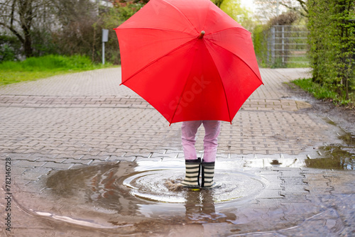 mischievous 5-year-old girl in rubber boots with red umbrella stands in rain puddle  capturing pure and simple joys childhood and magic rainy day