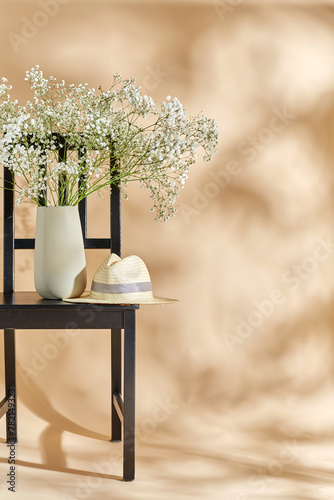 home decor and design concept - close up of gypsophila flowers in vase and straw hat on vintage chair over beige background © Syda Productions