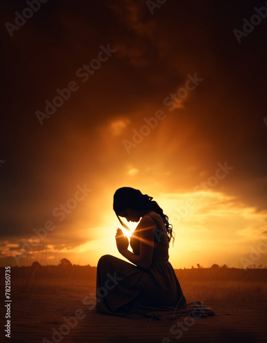 Prayer concept. Silhouette of a pretty woman in a praying pose. Set against a vibrant sunset sunrise sky. Clasped hands. Also related to communion, evangelism, evangelical, baptism, witness, proclame 