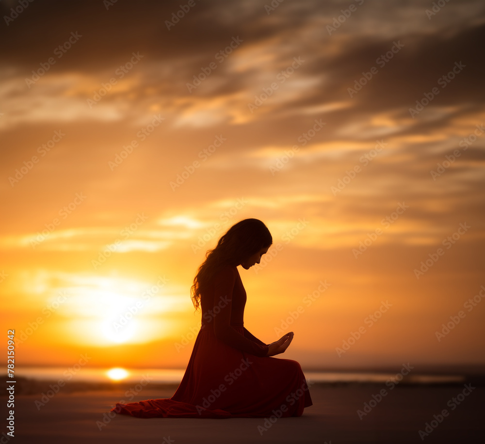 Prayer concept. Silhouette of a young woman in a praying pose. Set against a vibrant sunset sunrise sky. Clasped hands. Also ties in with heartfelt, inspiration, patience, tranquil, bless, resilient