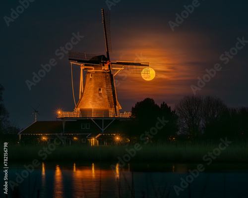 The full moon shines through the sails of the windmill. The full moon rises behind the Anna Paulowna windmill. The presence of wispy clouds softens the bright moonlight, creating a tranquil atmosphere photo