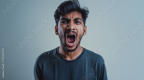 An Indian young man screaming out of frustrations against a light grey gradient background photo