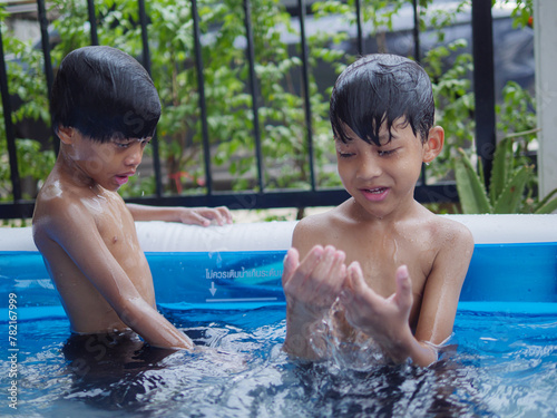 Two cute Asian children happily playing in an inflatable pool in summer. including jumping into the water, diving in the inflatable pond © Tanawit
