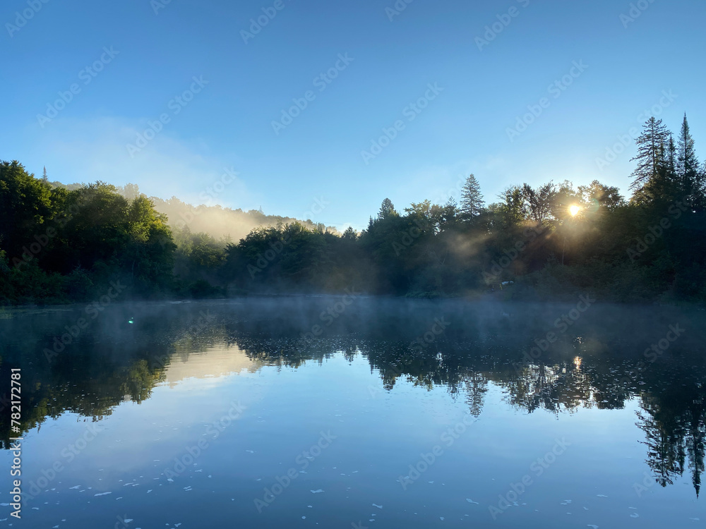 Morning on the river. Quiet forest and river at dawn. Reflection of a mountain on a lake in the early twilight. Sunrise with mist on the water. Sunbeams through the fog.