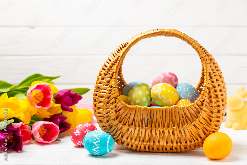 Easter basket filled with colorful eggs and a bouquet of tulips on a textured wooden table. Easter celebration concept. Colorful easter handmade decorated Easter eggs. Place for text. Copy space Easter basket filled with colorful eggs and a bouquet of tulips on a textured wooden table. Easter celebration concept. Colorful easter handmade decorated Easter eggs. Place for text. Copy space