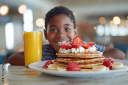 n African American boy with a joyful smile having pancakes and a glass of orange juice.
