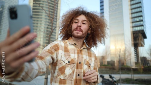 young adult with curly hair takes selfie for online dating application with his mobile phone