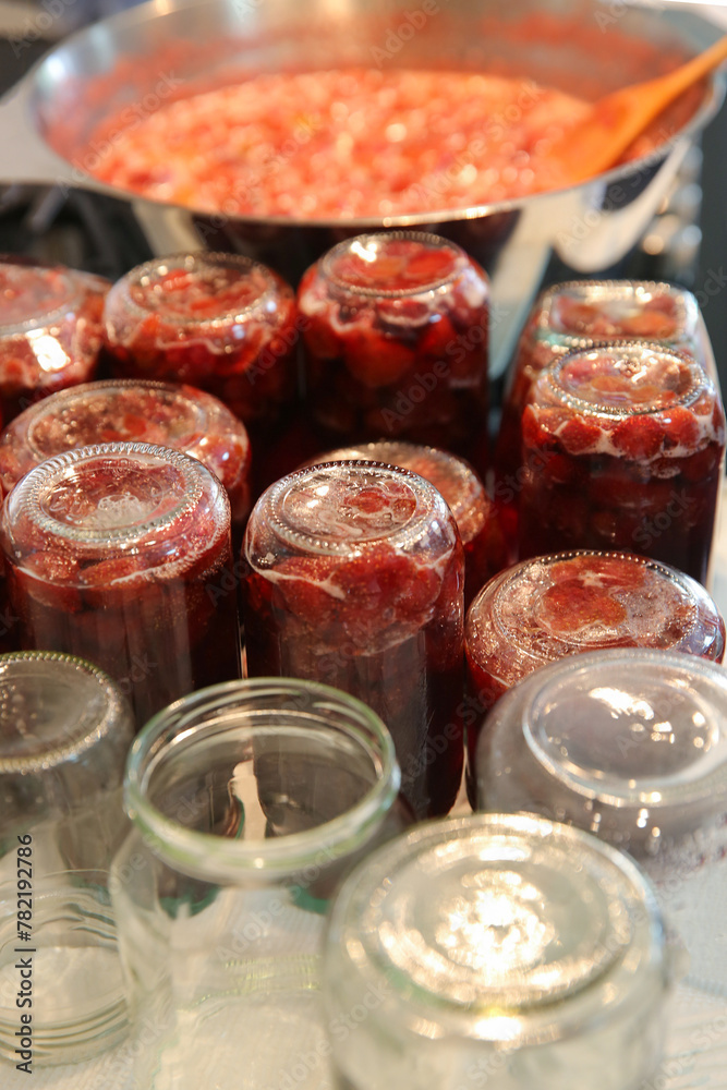 Cooking strawberry jam in a large bowl at home. Wooden spoon in a bowl with jam. Empty glass jam jars and jars filled with jam.