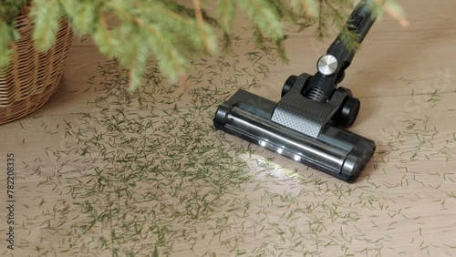 Close up modern wireless vacuum cleaner with illumination cleans needles under fir tree on laminate floor in apartment. Keeping house neat at home after holidays. House cleaning , housework concept
