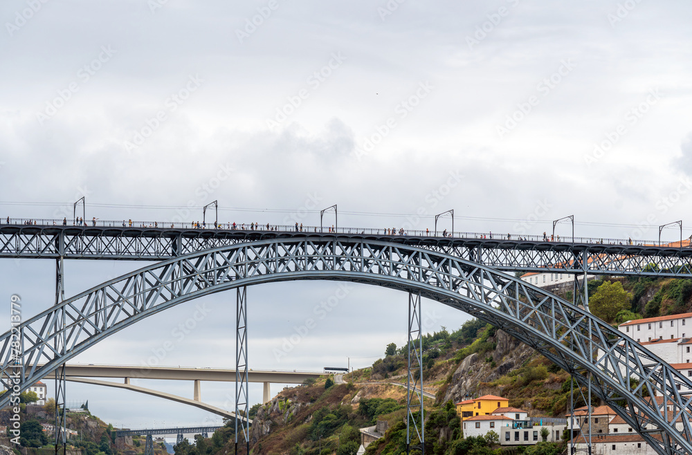 Fototapeta premium Frontal view from the river of the Don Luis I steel bridge with people walking, taking photos and posing and three other bridges in the background of the Douro River in Porto. Lisbon.