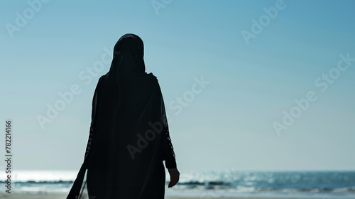 A serene Muslim woman in hijab strolls peacefully along the sunny shoreline