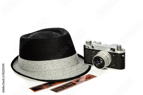 A mans black fedora hat with a white band with an old 35 millimeter film camera and some exposed film strips  isolated on white