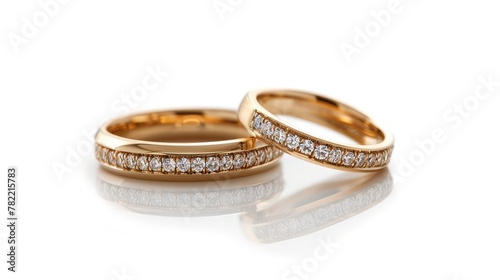 An isolated image of a pair of golden wedding bands with diamonds. On a white background with soft reflections.