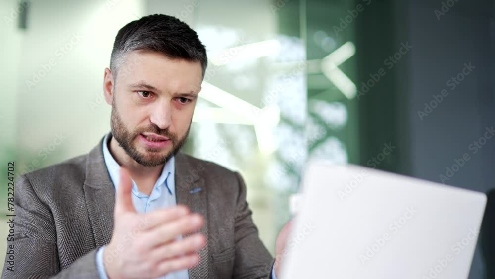 Confident businessman talking on a video call using a laptop computer sitting at workplace in office. A man worker has a business meeting, speaks remotely, communicates at online conference. Close up Confident businessman talking on a video call using a laptop computer sitting at workplace in office. A man worker has a business meeting, speaks remotely, communicates at online conference. Close up