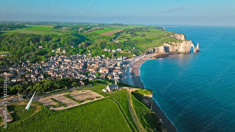 Aerial view of French traditional houses by the towering cliffs and natural arch in Etretat in France. Rock formation by the water edge, scenic point tourist attraction. Scenic view of Falaise d'Aval.