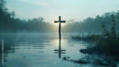 Solitary wooden cross partially submerged in tranquil water with ripples, surrounded by greenery, conveying a sense of peace, faith, and reflection. photo