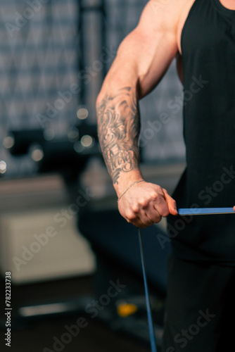close up in the gym a young handsome guy with tattoos in a black T-shirt does exercises with an elastic band