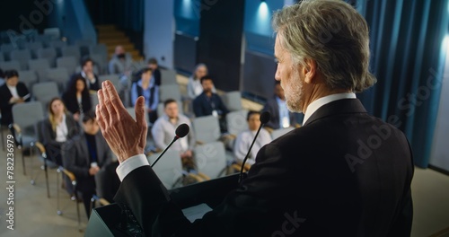 Back view of politician or activist pronouncing speech during press campaign in the conference hall. Mature organization representative answers questions, gives interview to journalists for media.