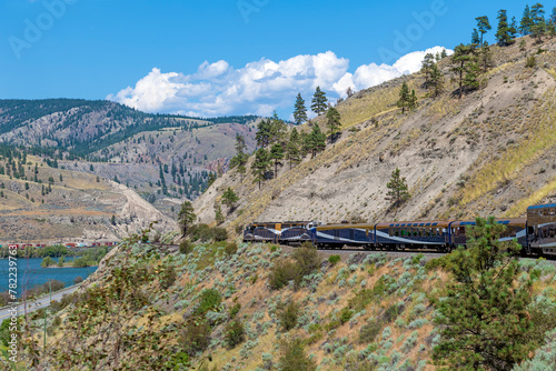 Rocky mountaineer locomotive with gold and silver leaf train wagons along Fraser River, British Columbia, Canada