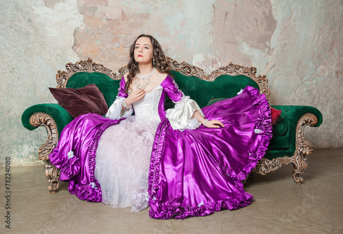 Young serious beautiful woman in fantasy rococo style medieval dress sitting on the sofa