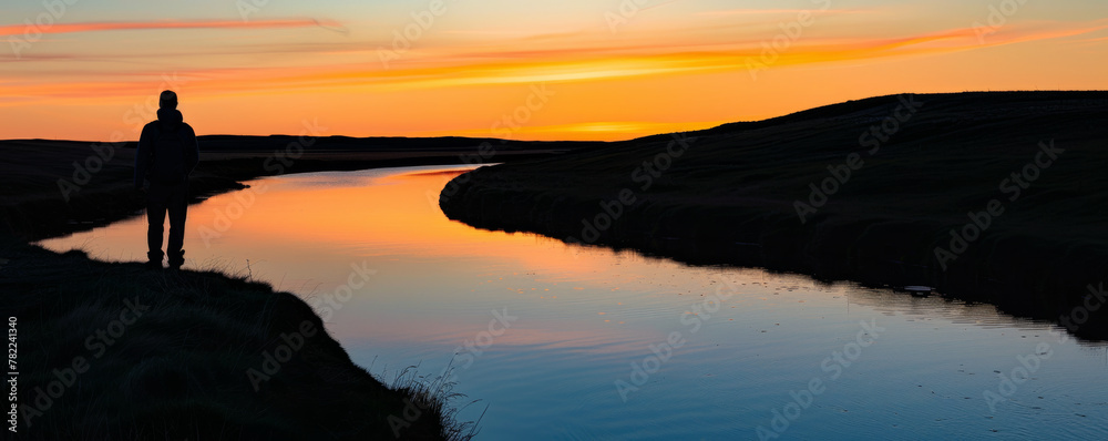 Silhouette of a person standing by a river at sunset Silhouette of a person standing by a river at sunset