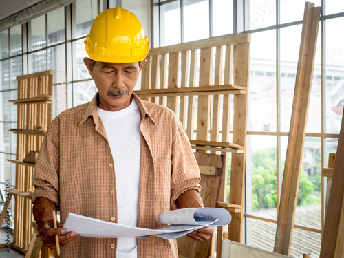 Portrait of a senior carpenter looking at blueprints plans, rechecking and comparing drawing plans. Hobby, Retirement Concept photo