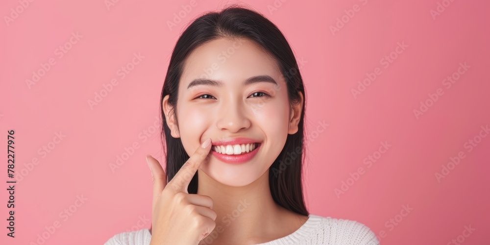Beautiful young Asian woman pointing finger to her teeth on pink background. Facial and skin care concept for commercial advertising. Beautiful young Asian woman pointing finger to her teeth on pink background. Facial and skin care concept for commercial advertising.