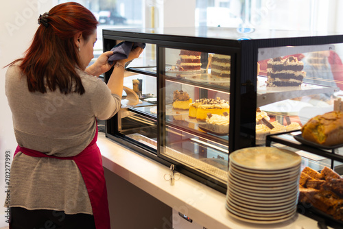 red-haired bakery owner cleans the display case of the artisan cakes and pies counter in her business