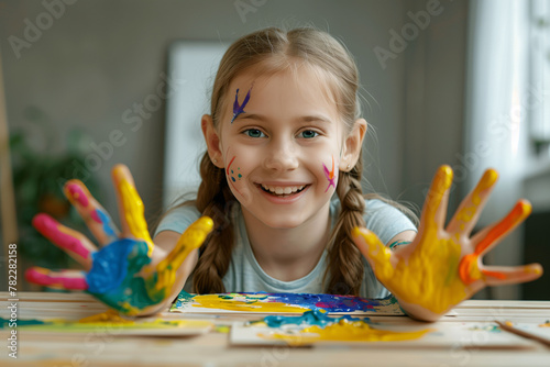 Cute portrait of a happy girl with her face and palms of her hands stained with colorful paint. Childhood, games and fun.