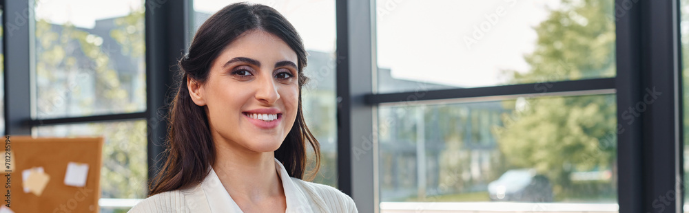 A businesswoman stands in front of a window, smiling brightly as sunlight illuminates her face, embodying a sense of empowerment and positivity. A businesswoman stands in front of a window, smiling brightly as sunlight illuminates her face, embodying a sense of empowerment and positivity.