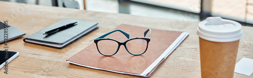 A pair of glasses rests on a vibrant notebook next to a steaming cup of coffee, set in a modern office workspace.