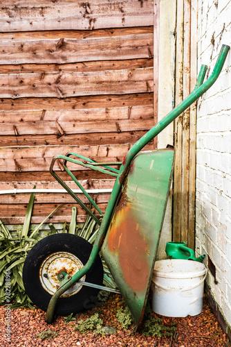green wheel barrow with orange rust leaning against the wall in the garden.