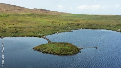 Eilean Domhnuill islet in Loch Olabhat, N. Uist, Scotland. Important 5000 year prehistoric Neolithic early crannog habitation site and causeway. View to S.W. Video aerial drone moving forward and down photo