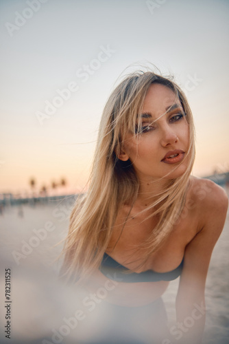 A woman stands confidently in an urban scene during sunset, hair blowing