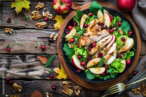 Fall salad with chicken apples nuts and cranberries on wood table