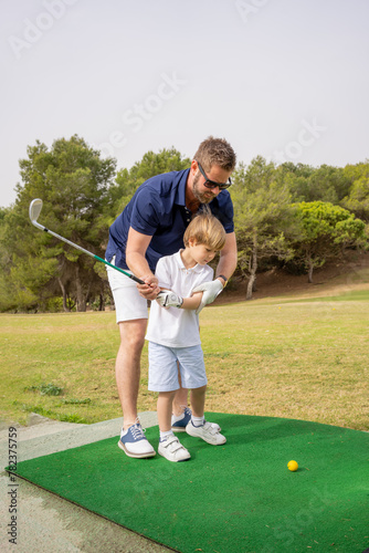 Portrait of young handsome father teaching his little son how to play golf