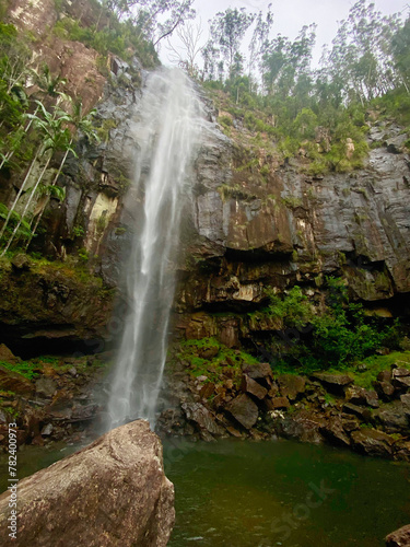 Beautiful waterfall with rock in the foreground and trees on the cliff edge