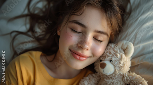 Satisfied happy teenager girl with brown hair in yellow casual T-shirt hugging cute white toy bear, closing eyes and dreaming, enjoying romantic gift. Indoor studio shot isolated on gray background.