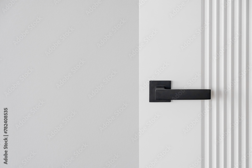 Obraz premium Modern black door handle on white wooden door in interior.