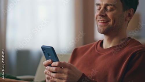 Positive guy texting mobile phone at home sofa close up. Cheerful man messaging