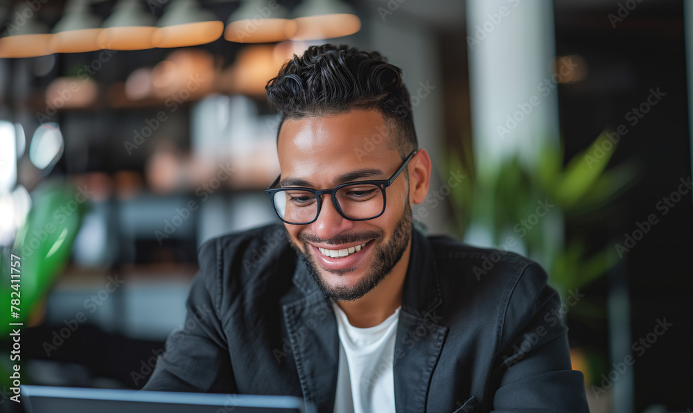 Obraz premium Young diverse successful businessman smiling while looking at laptop working on online project, eco friendly environment meeting office workplace.