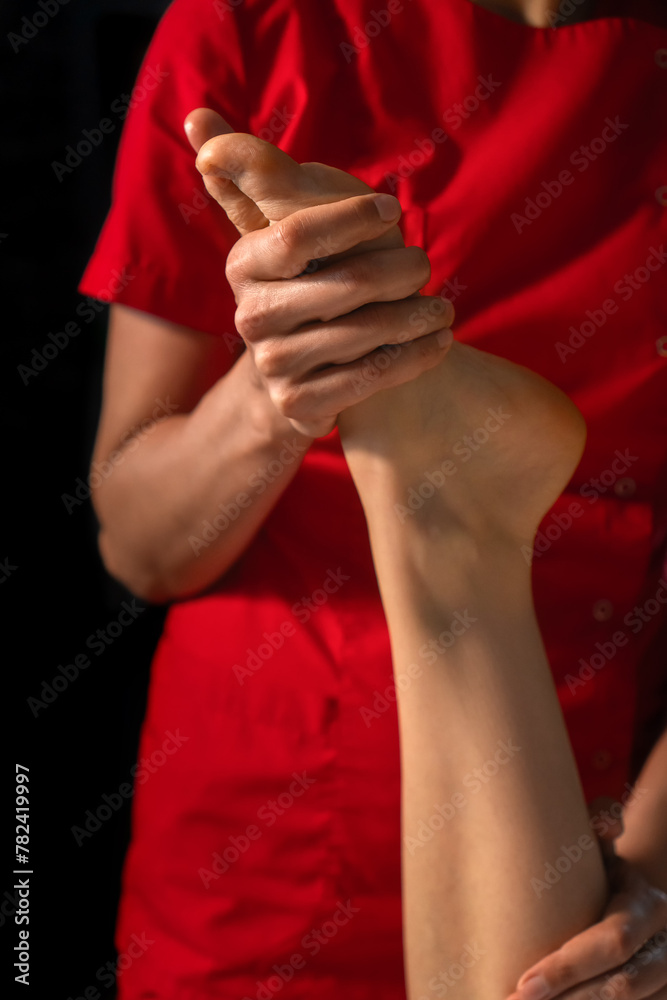 Close-up of a masseur in a red uniform doing foot massage to a young woman. Foot massage at the spa. Foot care. Vertical photo Close-up of a masseur in a red uniform doing foot massage to a young woman. Foot massage at the spa. Foot care. Vertical photo