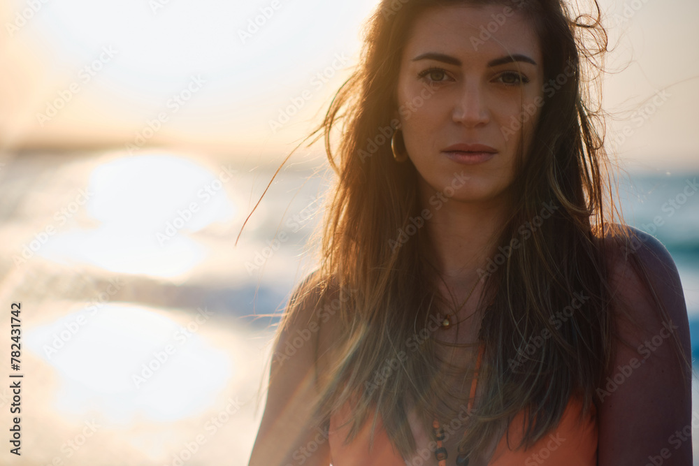 Woman's intense gaze with the beautiful sunset and ocean bokeh in the background Woman's intense gaze with the beautiful sunset and ocean bokeh in the background