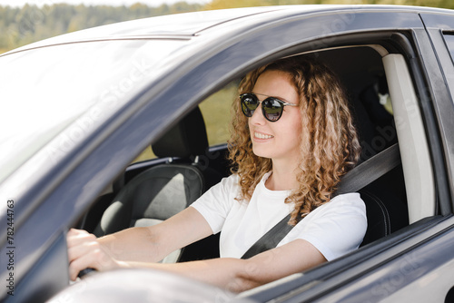 young beautiful smiling woman driving car, attractive caucasian woman in white t-shirt and black sunglasses