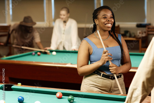 Waist up portrait of smiling African American woman chatting with friend while enjoying game of pool together in low light copy space