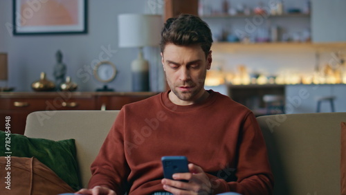 Disappointed freelancer reading smartphone message on apartment sofa close up