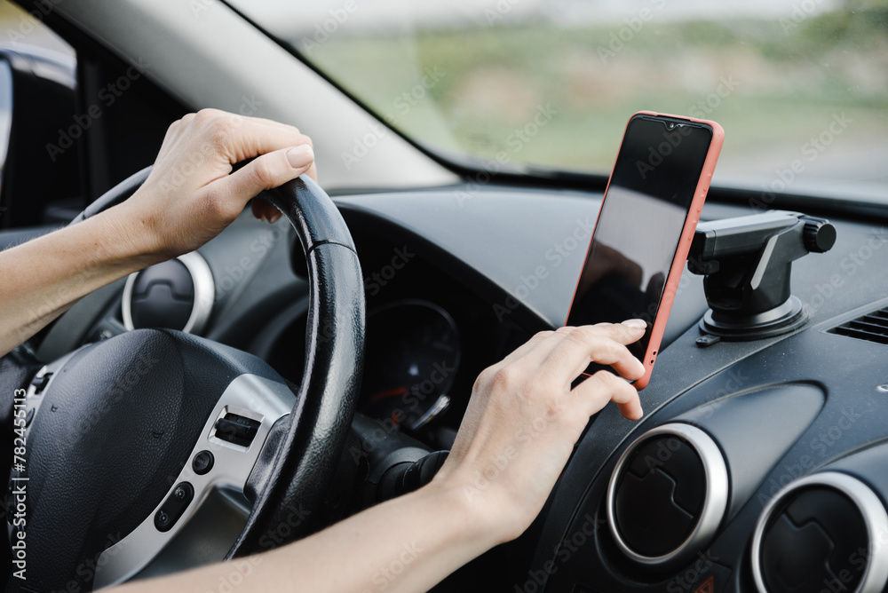 close-up view of hands, young woman in car, hands on steering wheel and with smartphone
