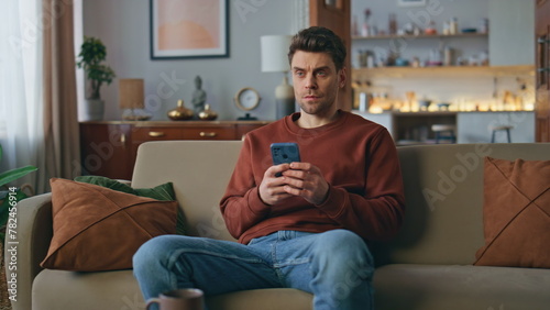 Frowning man looking mobile phone screen on cozy couch. Serious guy messaging © stockbusters