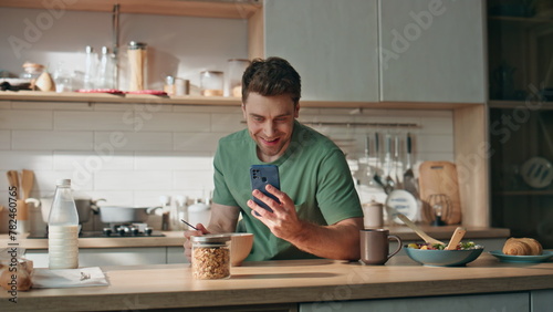 Happy man reading cellphone message kitchen counter closeup. Businessman eating