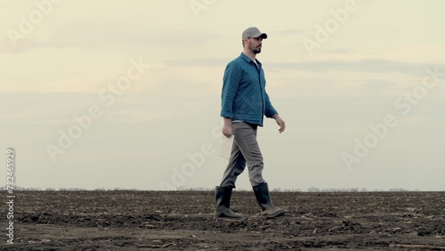 Farmer works with computer tablet in field sown in spring. Senior farmer walks on ground, assessing arable land in autumn. Agriculture. Smart farming technologies. Worker working on arable land